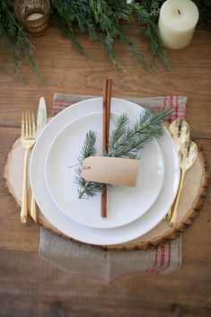 a table setting with white plates, silverware and greenery on top of it