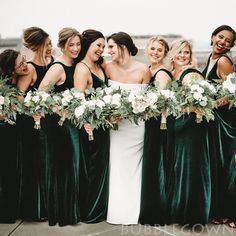 a group of women standing next to each other wearing green dresses and holding bouquets