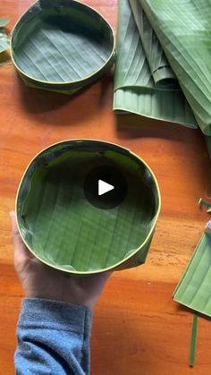 a person holding a green bowl on top of a wooden table next to banana leaves