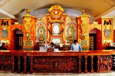 two people standing at the front desk of a large room with gold decorations on it