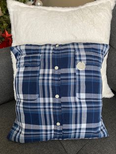 a blue and white plaid pillow sitting on top of a gray couch next to a christmas tree