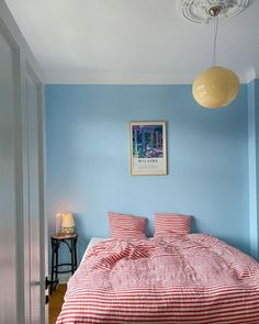 a bed with red and white sheets in a blue room next to a table lamp