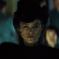 a woman wearing a black hat and dress in the dark with other people behind her