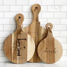 two wooden cutting boards with handwritten names are on a marble countertop next to a white brick wall