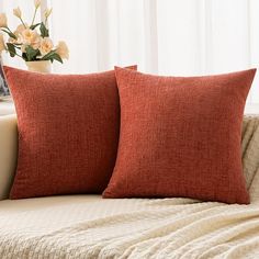 two red pillows sitting on top of a couch next to a vase with white flowers