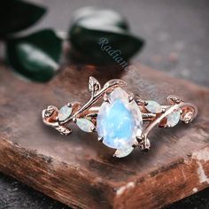 a close up of a ring on top of a wooden board with leaves and opal stones