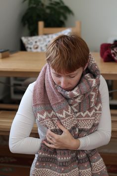 a woman wearing a knitted shawl and holding her hands on her chest while standing in front of a table