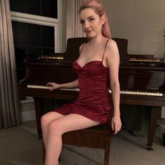 a woman in a red dress is sitting at a piano and posing for the camera