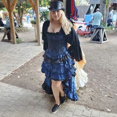 a woman in a blue dress and hat poses for the camera on a brick walkway