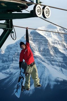 a snowboarder hanging from the side of a ski lift with mountains in the background