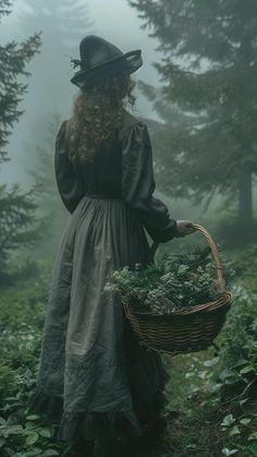 a woman in a long dress and hat carrying a basket full of plants on a foggy day