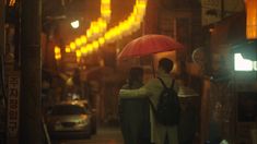 two people standing under an umbrella on a city street at night with traffic lights in the background