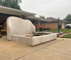 a bed frame sitting in the middle of a driveway next to a house with a car parked nearby