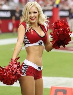 a woman in a red and white cheerleader outfit is standing on the football field