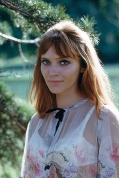 a woman standing in front of a tree wearing a shirt with flowers on the collar