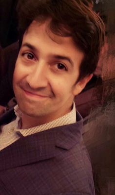 a young man smiling and wearing a purple sweater over a white shirt with black stripes