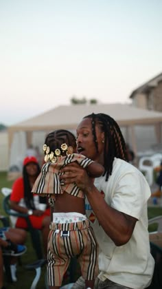 a woman holding a child in her arms with a red heart floating above it and people sitting on lawn chairs