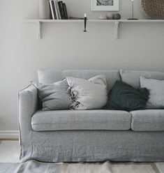 a gray couch with pillows on it in front of a white wall and some bookshelves