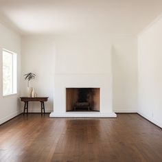 an empty living room with wood floors and a fireplace in the center, surrounded by white walls