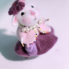 a small stuffed animal with pearls on it's neck and legs sitting on a purple object