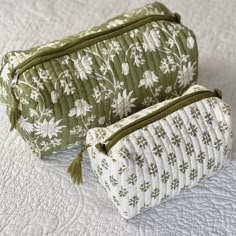 two green and white floral bags sitting on top of a quilted bedspread