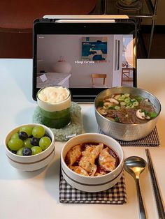 a laptop computer sitting on top of a table next to bowls of food