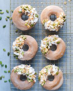 four doughnuts with frosting and toppings on a cooling rack next to pistachio seeds