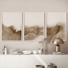 three paintings hanging on the wall above a white table with two vases and books