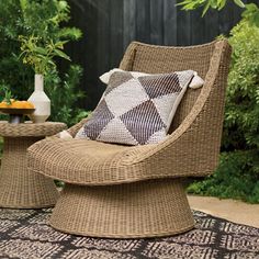 a wicker chair and table with pillows on it in a backyard area surrounded by plants