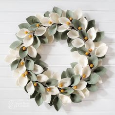 a wreath with white flowers and green leaves is hanging on the side of a wall