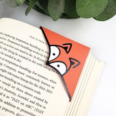 an orange bookmark with a red fox on it sitting next to a green plant