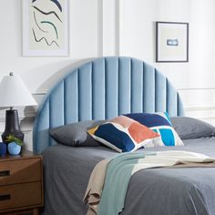 a bed with blue headboard and pillows in a white room next to a lamp