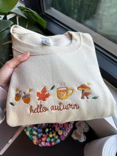 Hello Autumn Embroidered Sweatshirt! It couldn't be fall season without the perfect fall sweater! Embroidered on Gildan 50/50 Cotton/Polyester Blend. Using fall colors, our machine embroiders the cutest fall crewnecks! The perfect outfit for fall outings, watching movies, or going to the pumpkin patch! White Hoodie With Embroidered Graphics For Fall, Cute Custom Embroidered Tops For Fall, Cute Tops With Custom Embroidery For Fall, White Letter Embroidery Sweatshirt For Fall, Embroidered Long Sleeve Sweater For Fall, White Cotton Fall Sweatshirt, Cute Relaxed Fit Sweatshirt For Fall, Fall Embroidered Logo Long Sleeve Hoodie, Fall Hoodie With Embroidered Logo And Long Sleeves