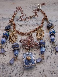 An assemblage of vintage components in a Bohemian style. The central assembled pendant is a vintage to antique fleur dis lis shape copper over brass component to which I've added a vintage German glass intaglio of the Eiffel Tower on the back. It suspends an Art Deco faceted blue glass cabochon in a filigree silver setting. Originally, this pendant would have had a rhinestone in the center, but it was missing, so I've added a gold plated brass filigree bead cap as a focal and to tie it in with the other brass elements in the design. Accompanying pendants are vintage Czech glass buttons, vintage Czech atlas glass and fire polished tulip shaped beads, Japanese 1930s glass beads and vintage lampwork beads with floral detail along with vintage caps and rhinestone rondelles. Length can be adjus Artisan Gold Jewelry With Vintage Charm, Vintage Patina Pendant Jewelry, Artisan Vintage Charm Necklaces, Artisan Necklaces With Vintage Charm, Ornate Decorative Necklaces For Vintage Style, Ornate Decorative Necklaces For Vintage Collection, Ornate Antique-finish Copper Jewelry, Ornate Antique Finish Copper Jewelry, Ornate Bronze Copper Jewelry