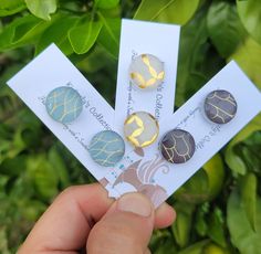 a person holding four different colored buttons in their hand and some green leaves behind them