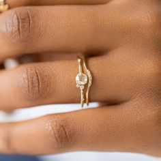 a woman's hand wearing a gold ring with a white diamond in the middle