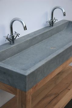 a concrete sink with two faucets on each side and a wooden shelf underneath