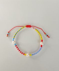 two bracelets with colorful beads and pearls on a white surface, one has a red string