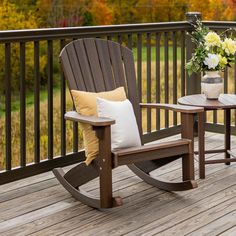 two rocking chairs on a wooden deck with flowers in the vase and potted plant