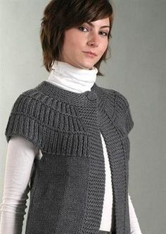 a woman wearing a gray knitted vest and white turtle - neck sweater is posing for the camera