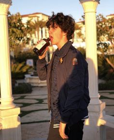 a young man drinking from a bottle while standing in front of a gazebo with palm trees