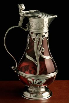 a silver and red glass pitcher sitting on top of a wooden table in front of a black background