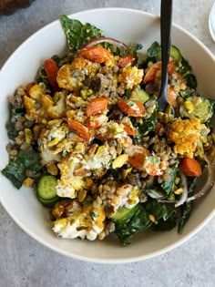 a white bowl filled with salad and vegetables on top of a table next to a fork