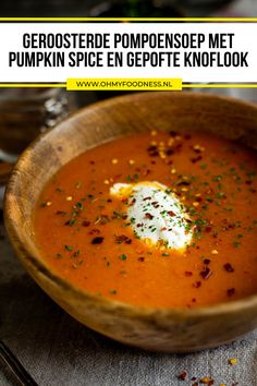 a wooden bowl filled with carrot soup and topped with sour cream on top, sitting on a table