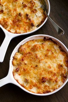 two white casserole dishes with cheese and meat in them on a wooden table