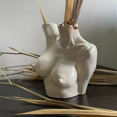 a white vase sitting on top of a wooden table next to dried grass and reeds