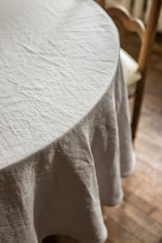 a round table with two chairs and a white table cloth draped over the top, on a wooden floor