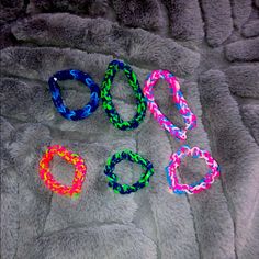 four different colored bracelets laying on top of a gray fur covered bed next to each other