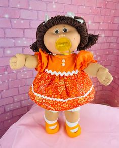 a doll with an orange dress and yellow pacifier in front of a brick wall