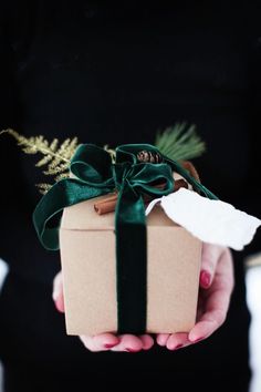 a person holding a brown box with a green ribbon on it and a pine branch